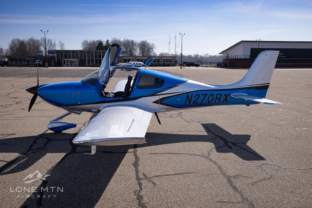 A side view of the blue and silver Cirrus SR20 aircraft, registration N270RX, parked on an airport tarmac with its doors open.