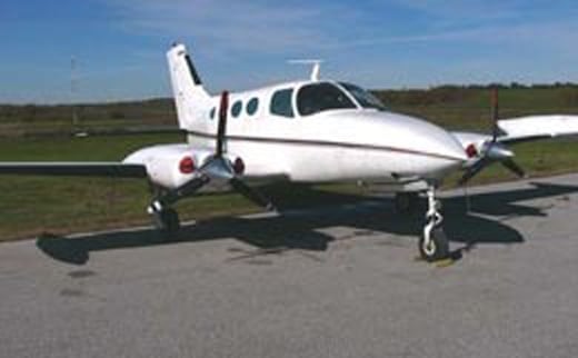 A white twin-engine aircraft parked on a runway.