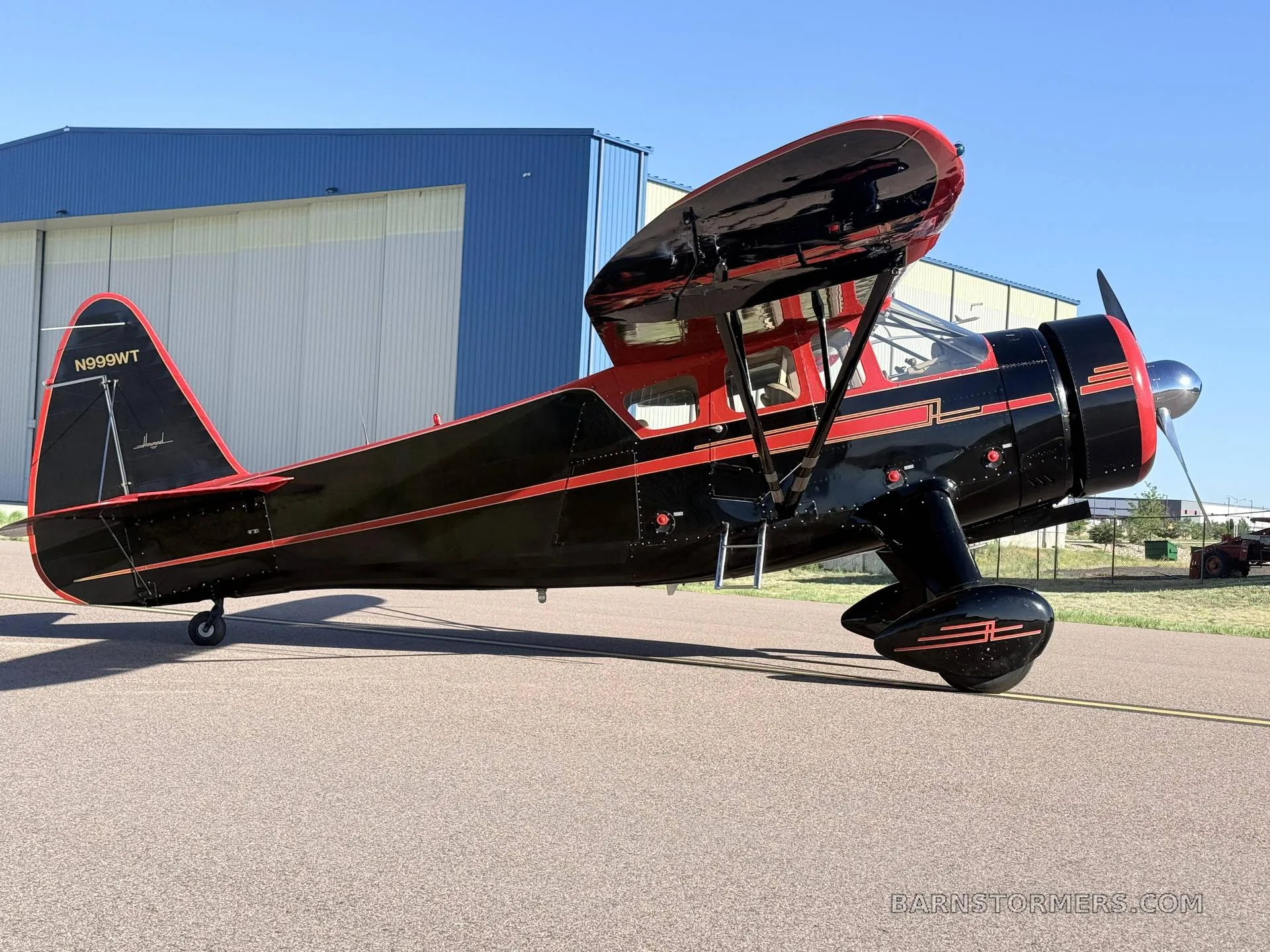 A side view of a black and red vintage high-wing monoplane with tail number N999WT, parked on an asphalt runway.