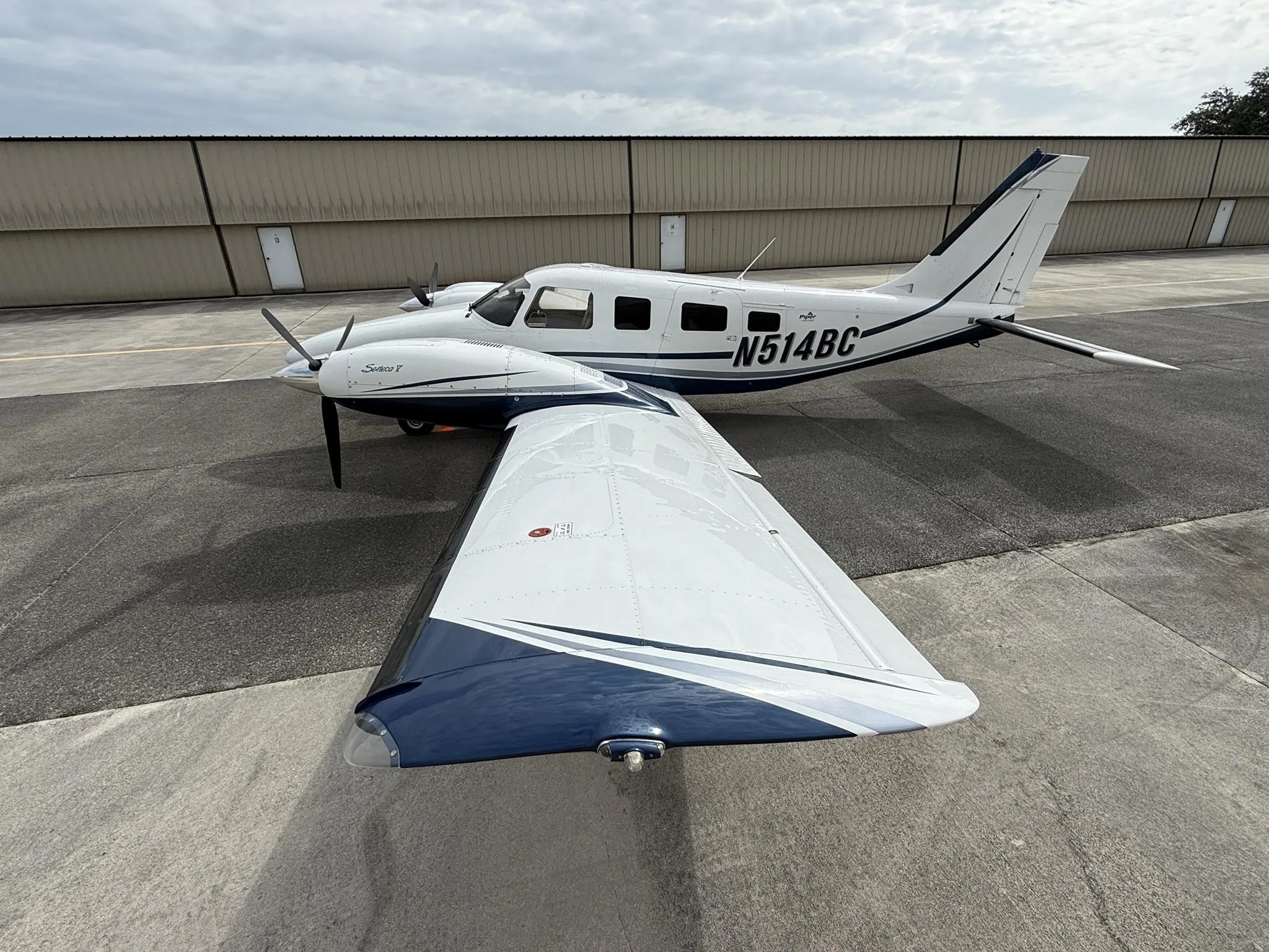 A white and blue Piper Seneca V aircraft, registration N514BC, parked on an airfield tarmac.