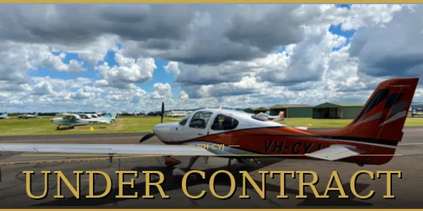 A white and orange single-engine piston aircraft, registration VH-CYJ, parked on a tarmac at an airfield under a cloudy sky.