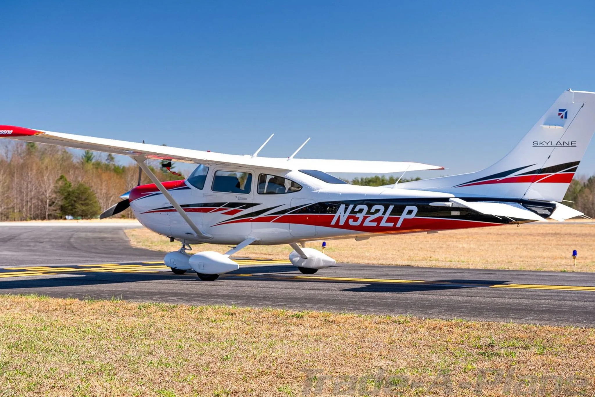 A white Cessna Skylane N32LP with red and black accents parked on a sunny tarmac, viewed from the left side.