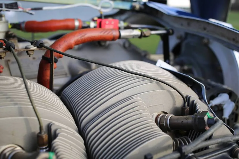 A close-up view of the gray finned cylinders and red hoses of an aircraft engine.