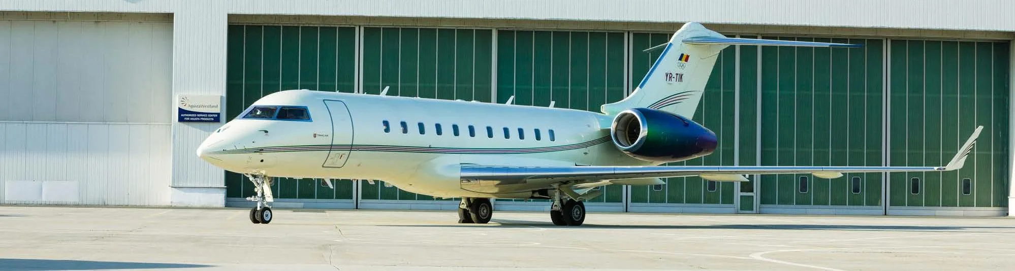 A grey Bombardier Global 5000 business jet flies over a blue ocean.