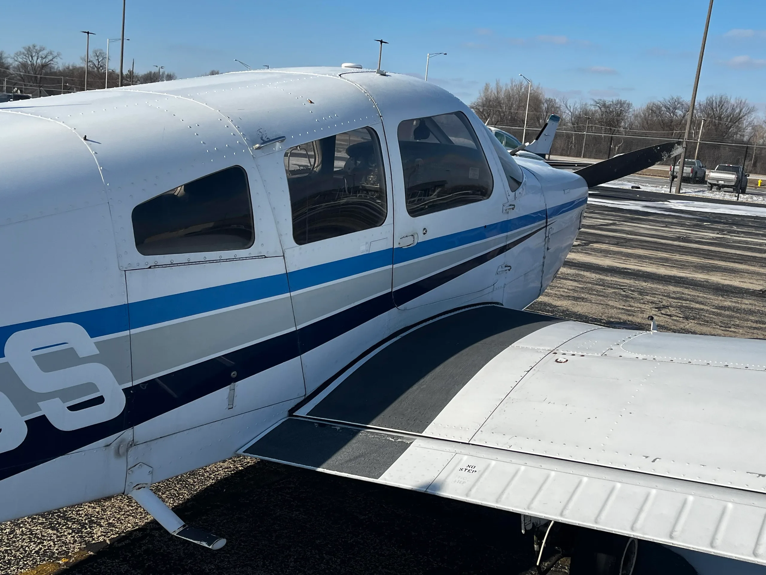 Close-up side view of a white single-engine propeller aircraft with blue and grey stripes.