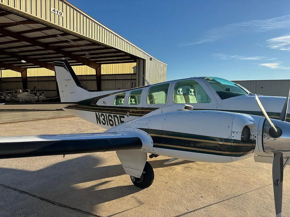 A white and green Beechcraft Baron N316DF parked on the tarmac next to a hangar.