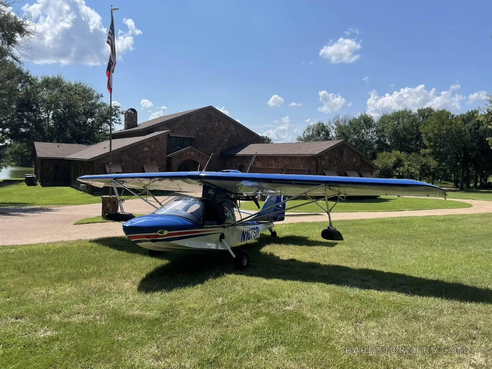 A blue and white Searey amphibian aircraft with registration N167SR parked on grass in front of a large stone building under a blue sky.