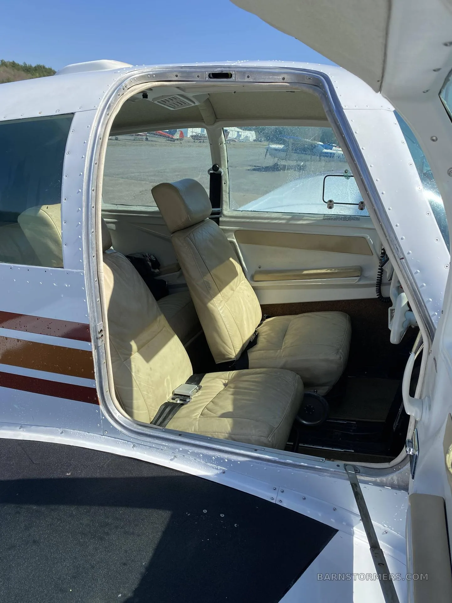 View into the light tan leather interior cabin of a small aircraft with an open door.