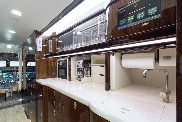 A well-equipped aircraft galley with a white countertop, sink, coffee maker, microwave, and a display screen.