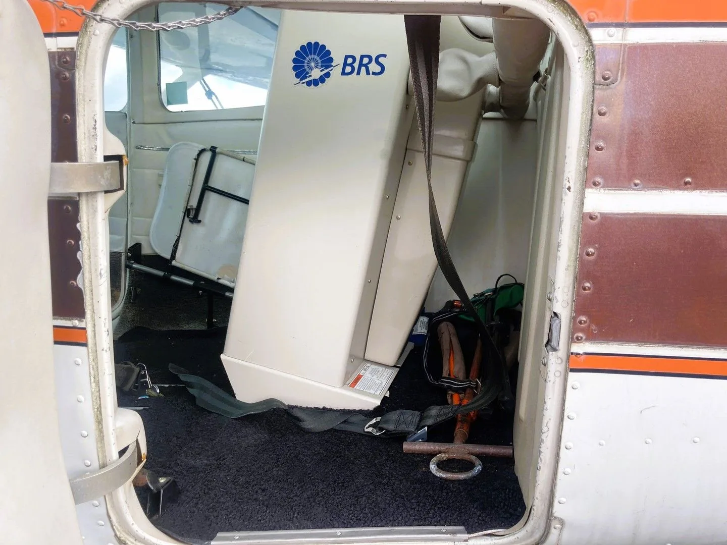 An interior view of the cargo area of a Cessna 182, showing a BRS parachute system and rear seats.