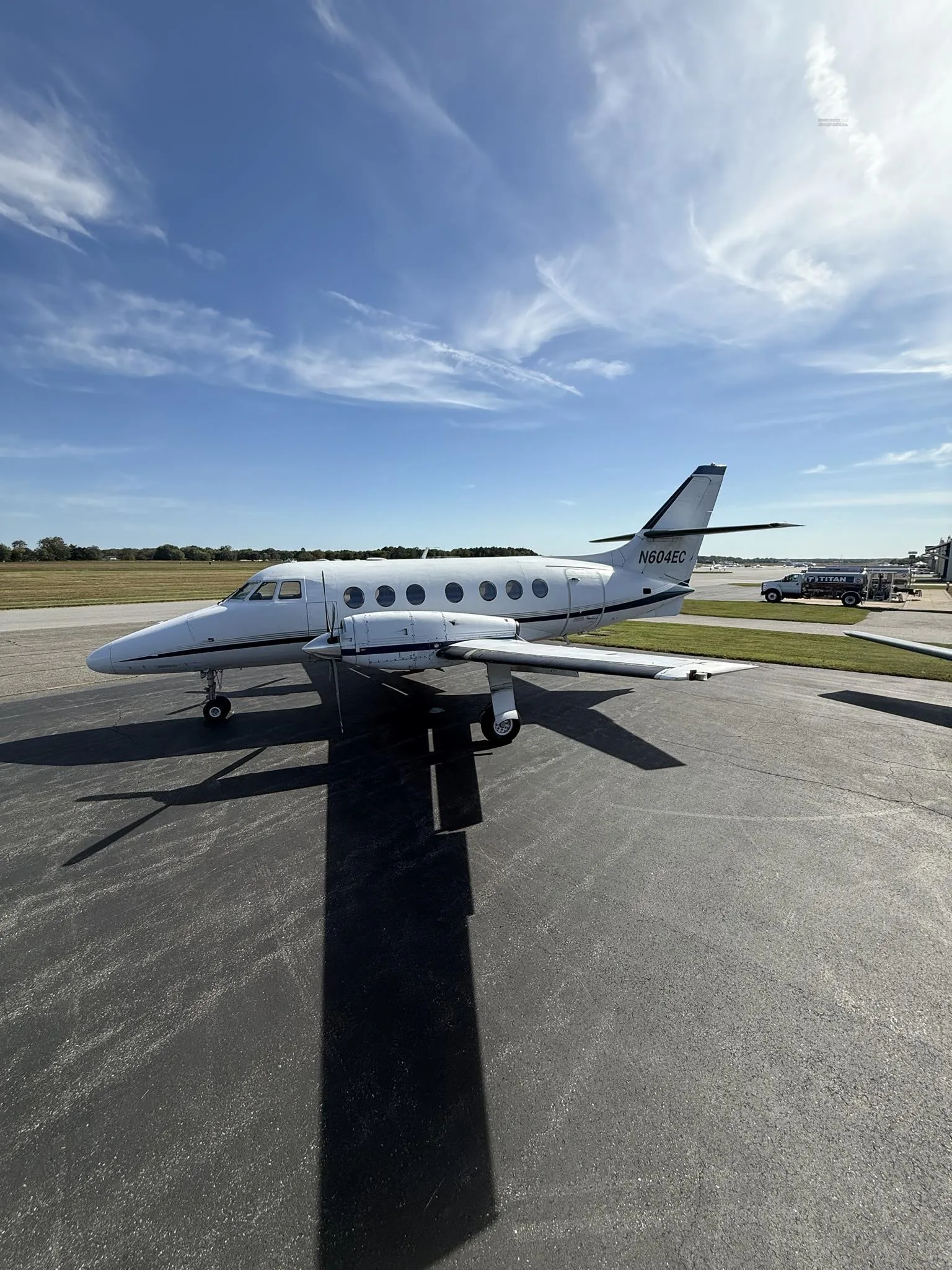 A white twin-turboprop aircraft, tail number N604EC, is parked on an asphalt tarmac under a blue sky.