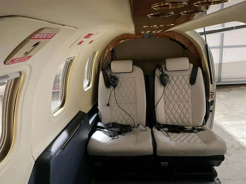 Two light-colored, diamond-stitched passenger seats with headsets in an aircraft cabin.