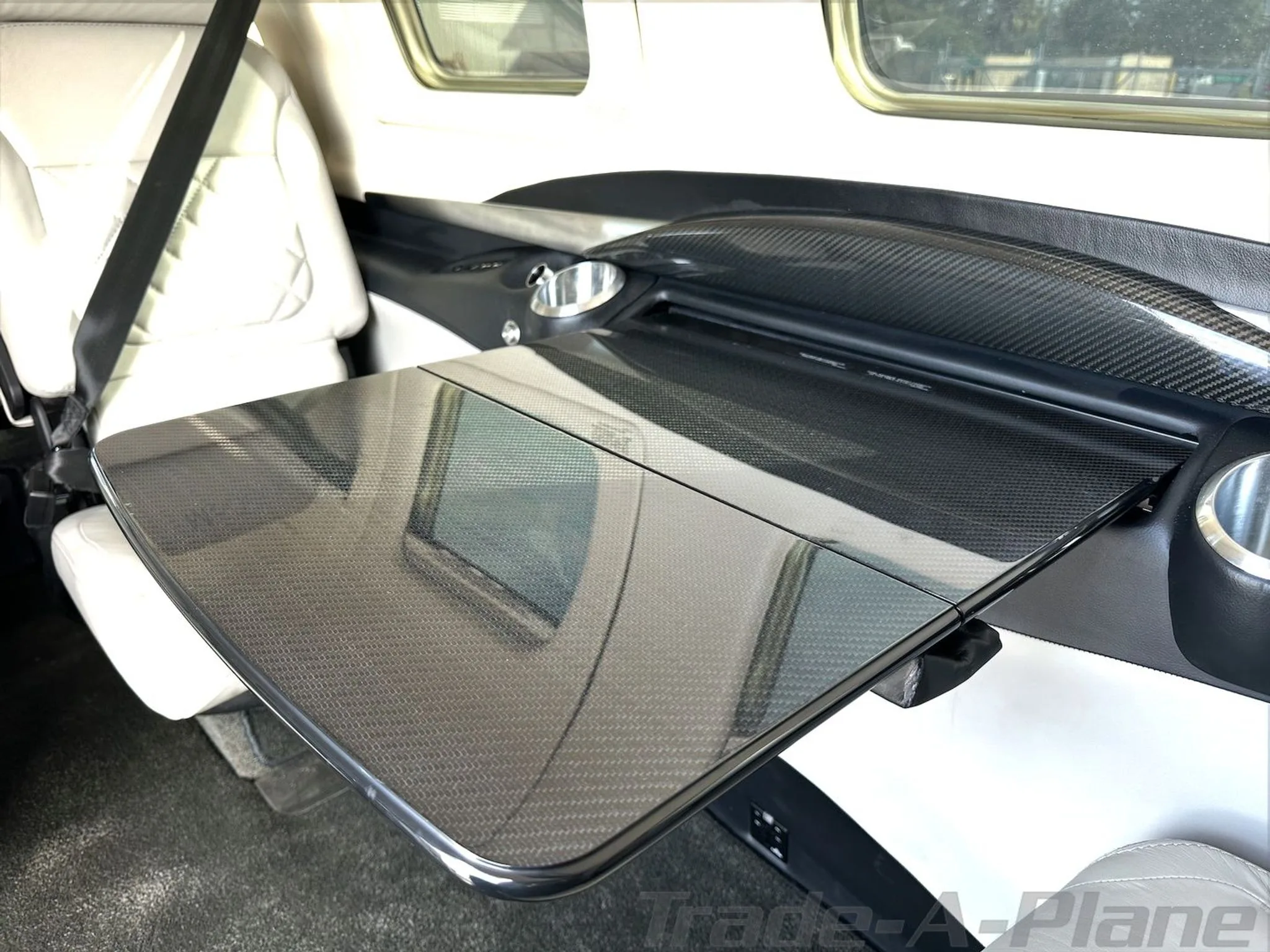 A close-up of the Piper M600/SLS cabin interior, showing a carbon fiber fold-out table and light-colored leather seats.