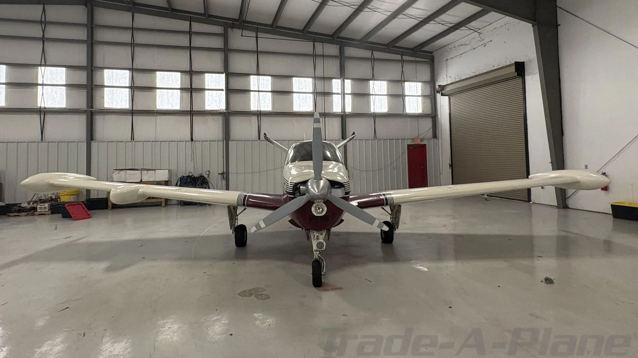 A white and maroon Beechcraft Bonanza N17VM parked inside a hangar, viewed head-on from the front.