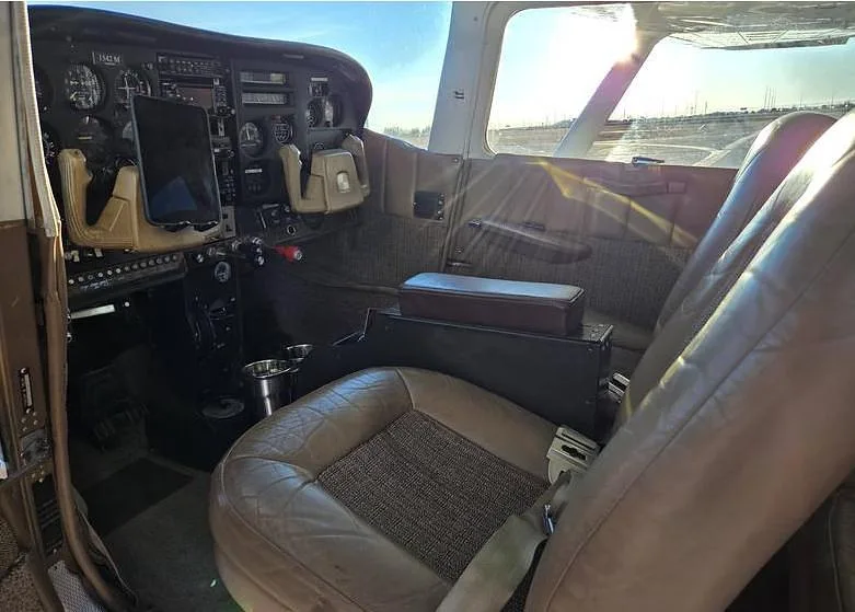 The cockpit and front cabin of a Cessna aircraft with brown leather seats and instrument panel visible.