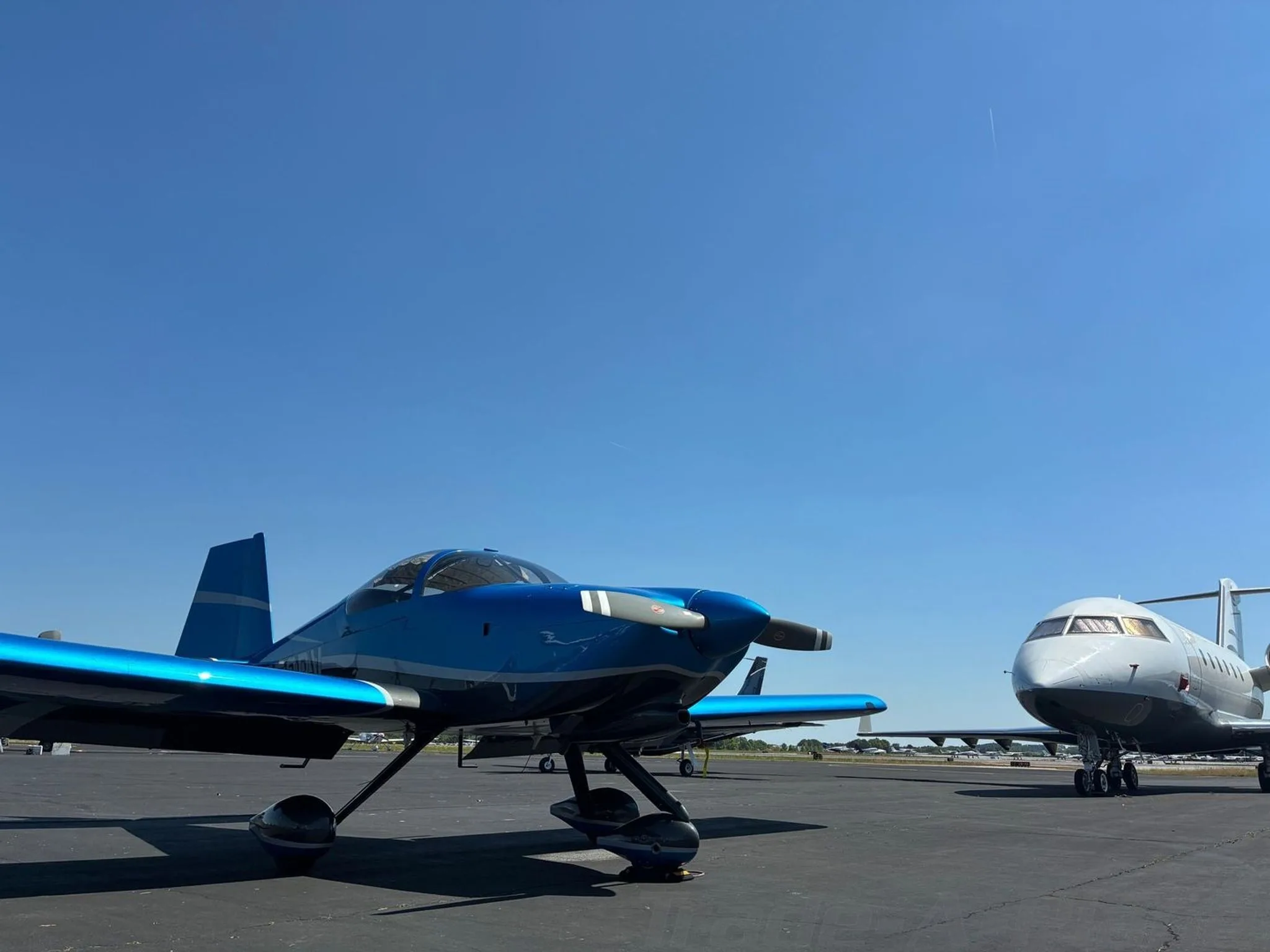 A blue and grey N853RV aircraft parked on an airfield with a larger white jet in the background.