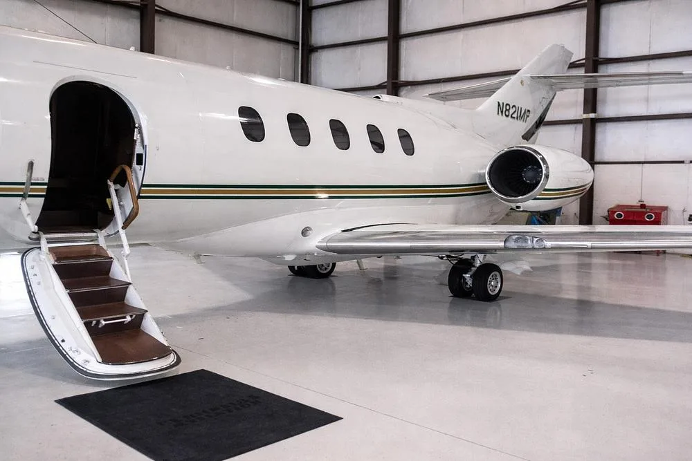 Side view of a white business jet, tail number N821MP, with green and gold stripes, parked in a hangar with its passenger door open and stairs extended.