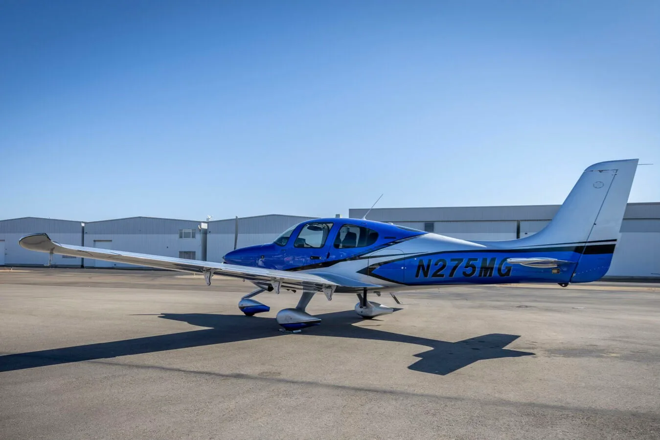 A side view of the blue and silver Cirrus SR22 aircraft, N275MG, parked on an airport tarmac.
