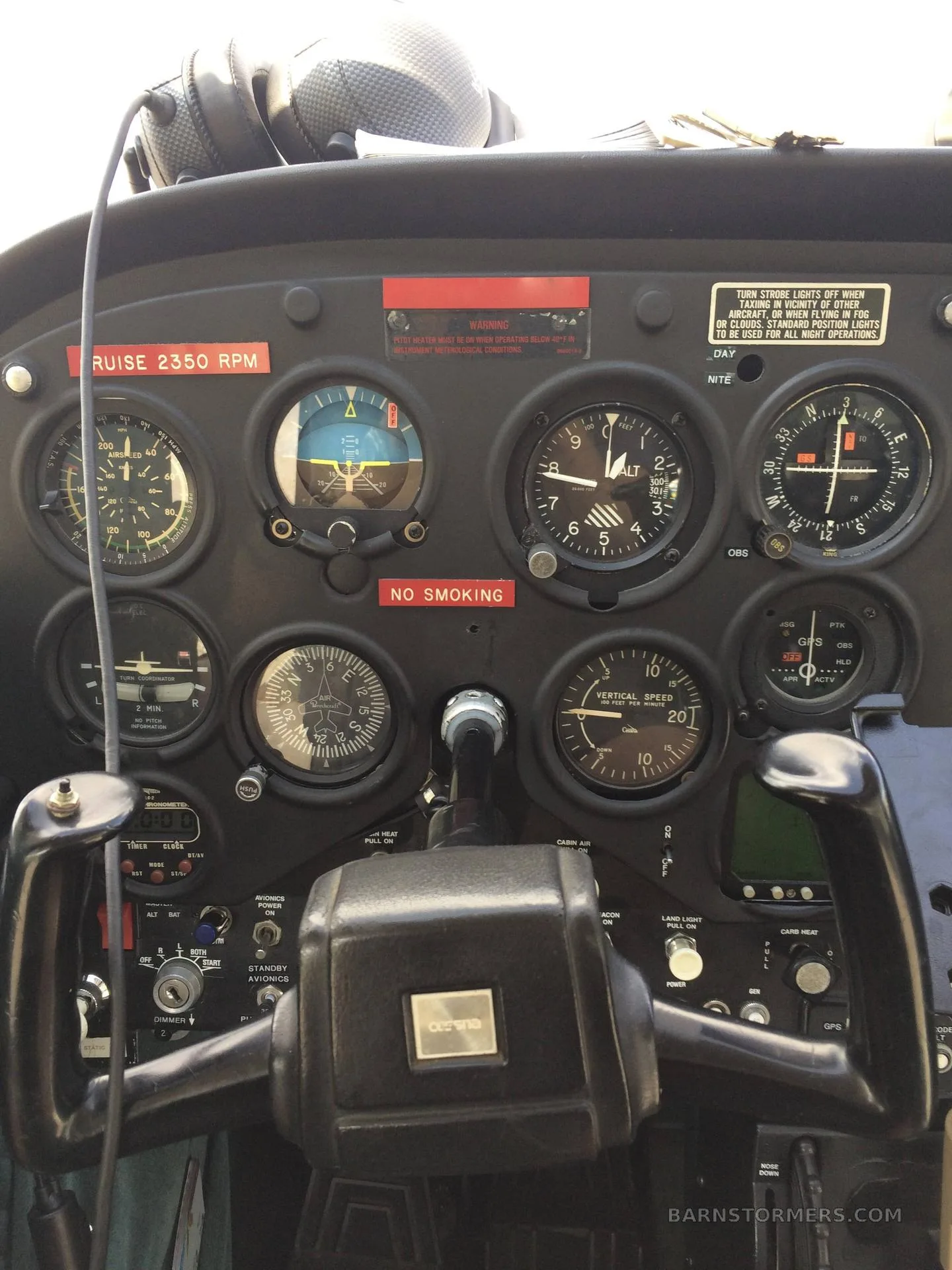 The cockpit instrument panel of a small aircraft with a black yoke and various gauges.