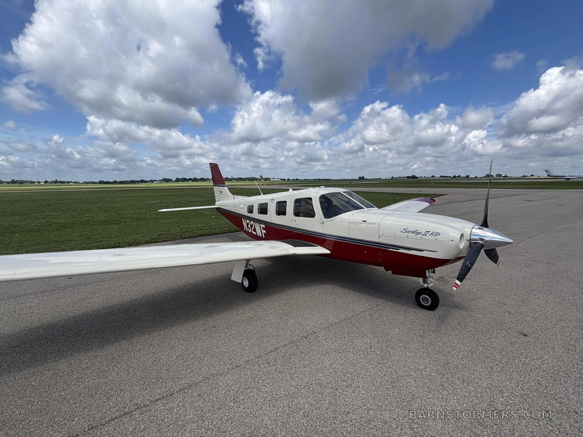 A white and red Piper Saratoga II HP aircraft (N32WF) is parked on an asphalt ramp under a partly cloudy sky.