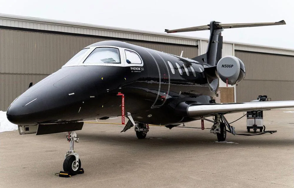 A close-up view of the front-right side of a black Embraer Phenom 300 jet (N506P) on the tarmac.