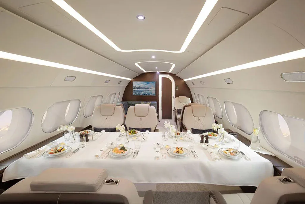 A private jet cabin configured for dining, with a long table covered in a white tablecloth and set with multiple place settings.