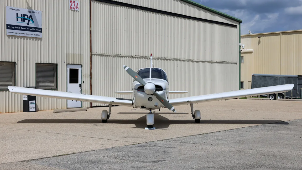 Front view of a white Piper Cherokee 180 (N9560J) with a two-blade propeller, parked on an airfield.