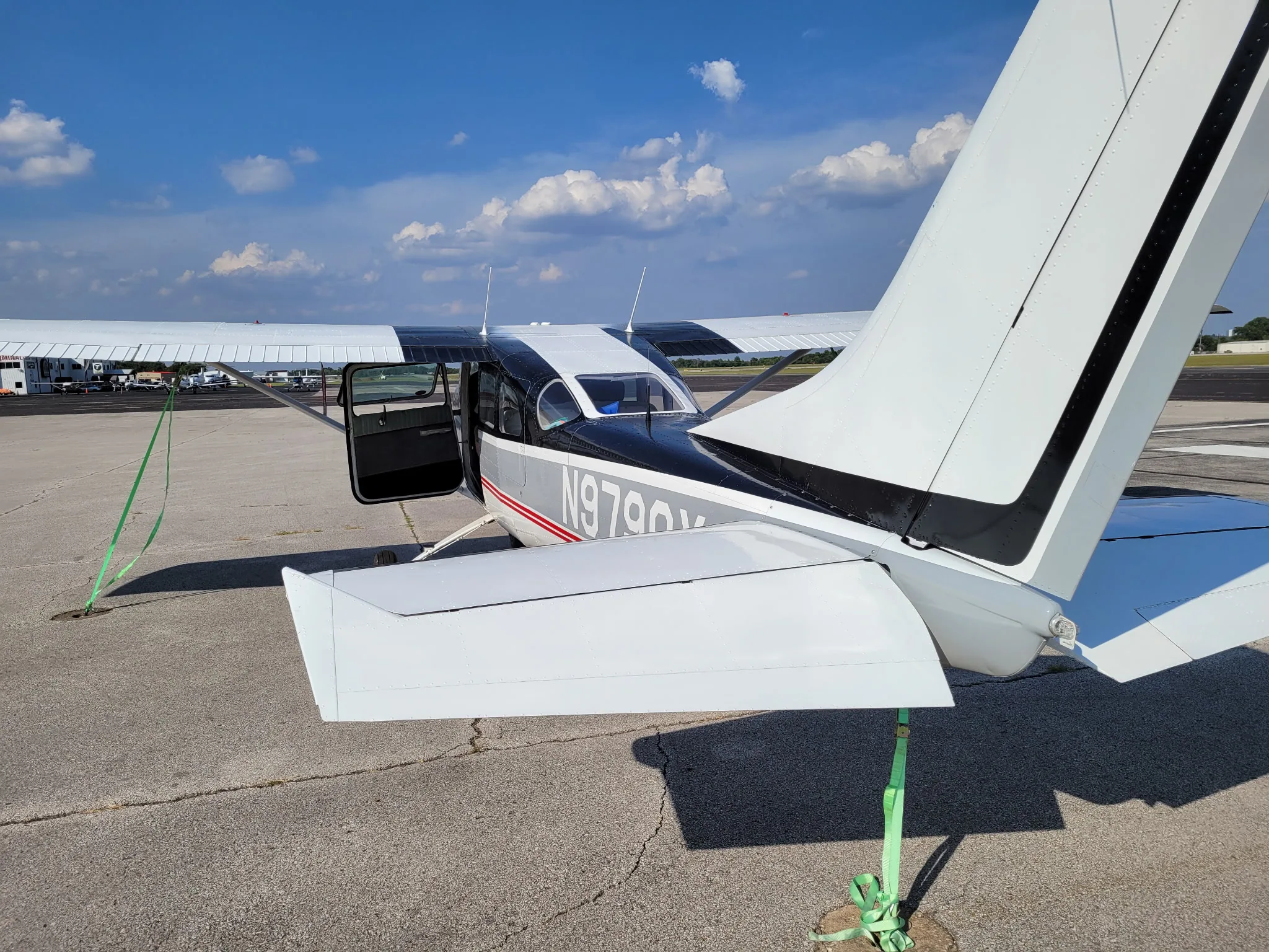 A black and white Cessna aircraft with registration N9790X is parked on an asphalt ramp with its door open, viewed from the rear.