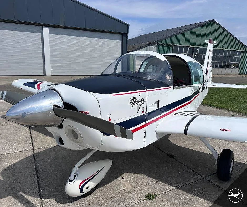 A close-up front-side view of the white Grumman AA-5B Tiger aircraft showing the propeller, nose, and cockpit canopy.