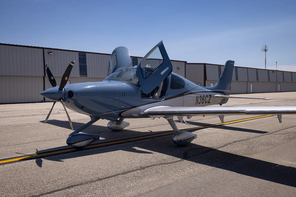 A blue and silver Cirrus SR22T aircraft with open doors parked on an airport tarmac.