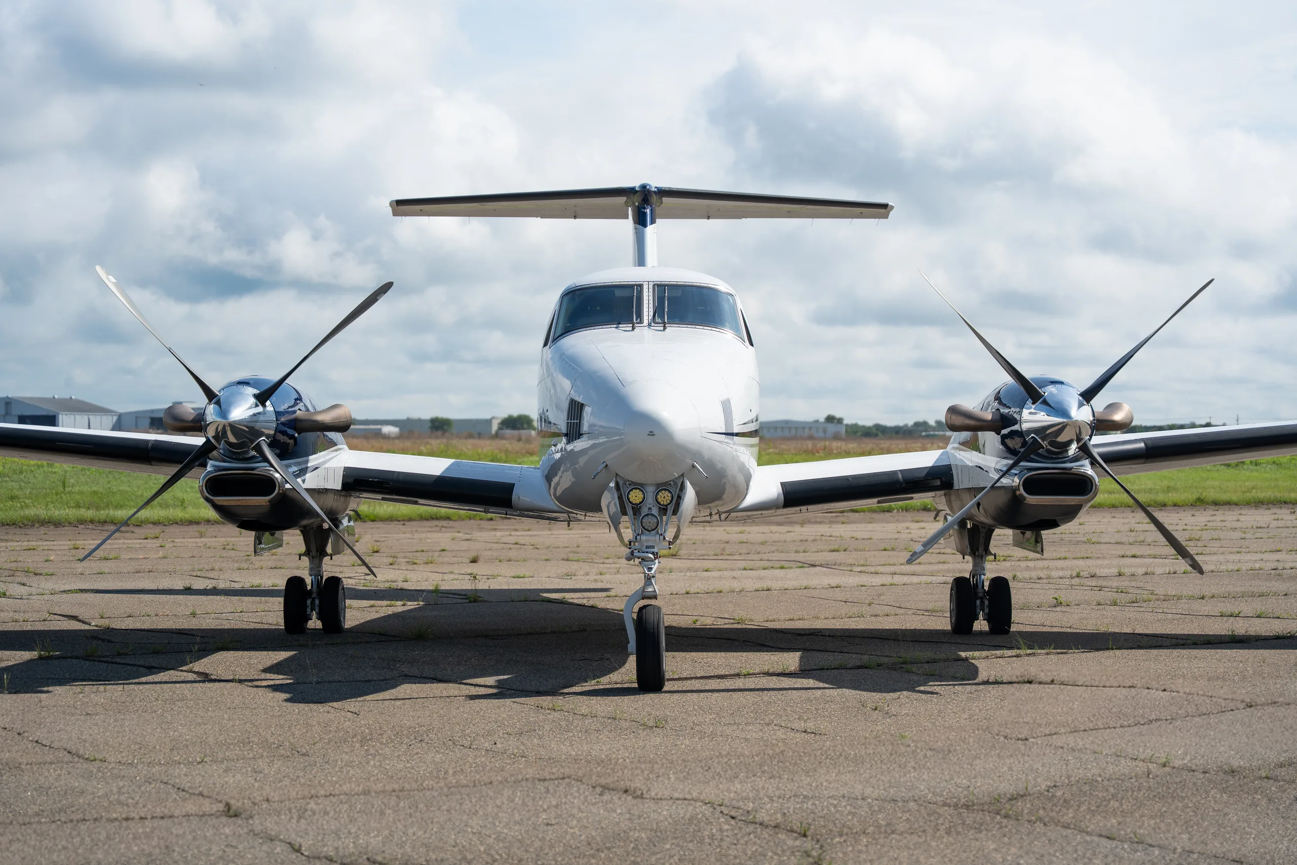 A head-on front view of a white and blue Beechcraft King Air twin-turboprop aircraft parked on a tarmac.