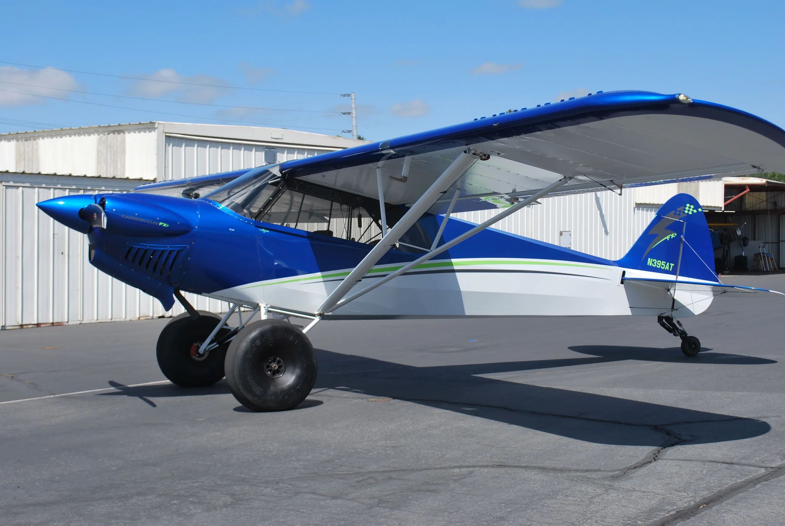 A blue and white Carbon Cub FX3 aircraft with large tires parked on an asphalt ramp.