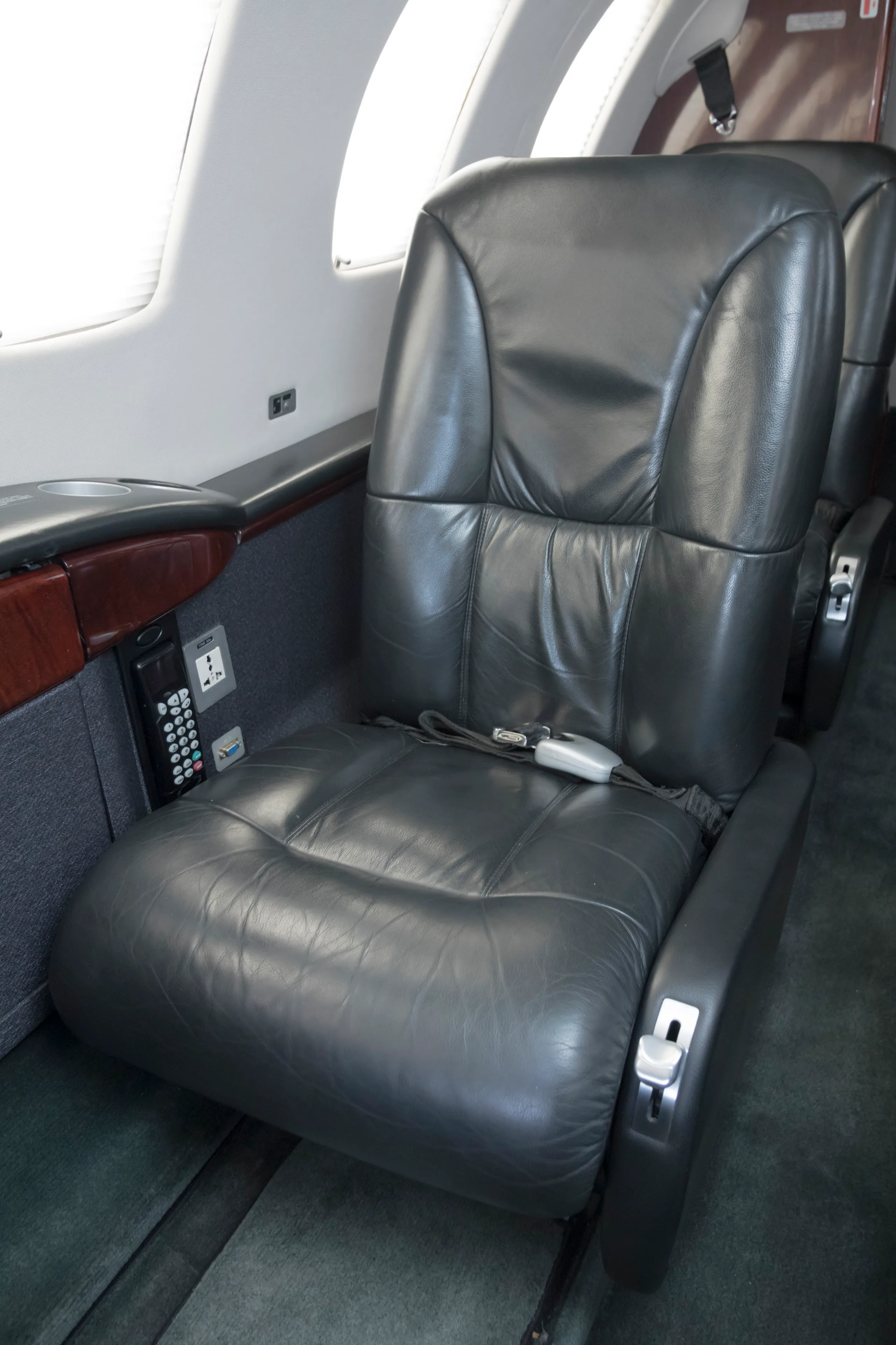 A close-up of a black leather passenger seat in a private jet cabin, with a control panel on the side.