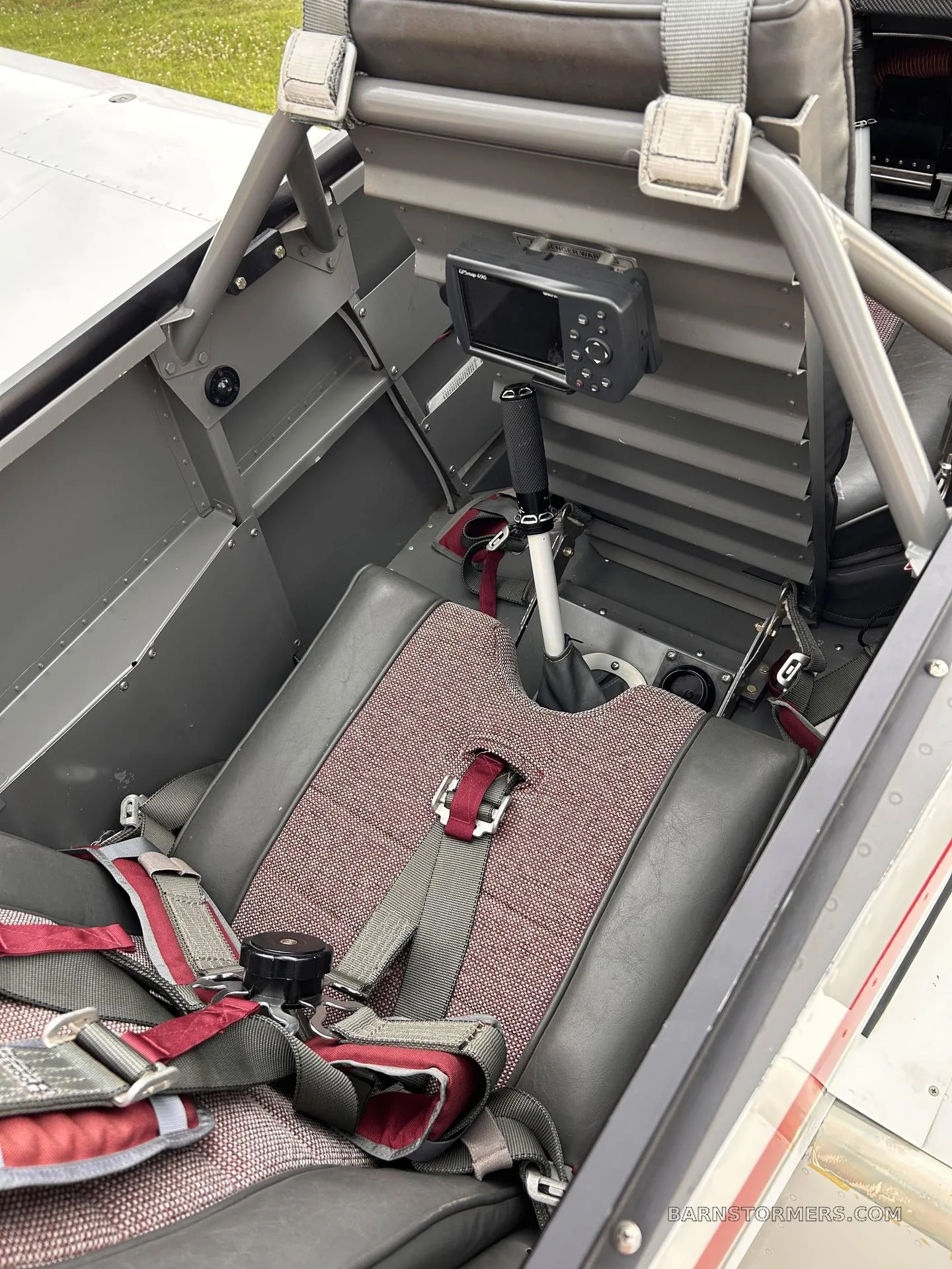 The single pilot's seat with a red and gray fabric pattern and a five-point harness in a light aircraft.