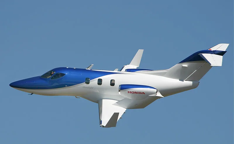A blue and white HondaJet in flight against a clear blue sky.