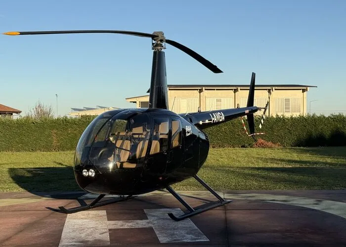 Robinson R44 helicopter with a black paint scheme parked on a helipad.