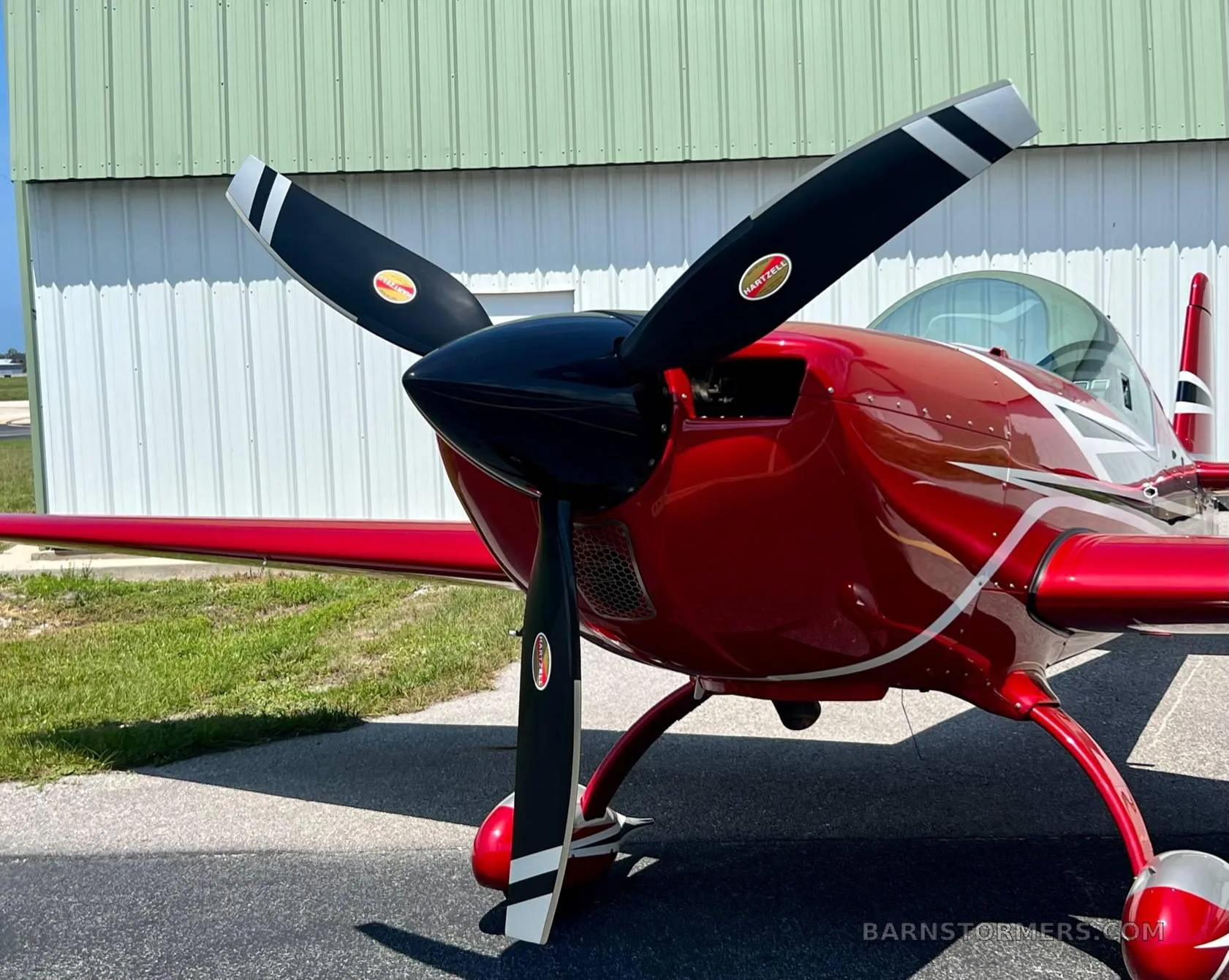 The front of a red and silver aerobatic aircraft highlights its black three-bladed propeller and sleek cowling.