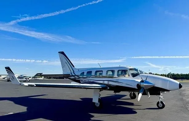A white and black twin-engine Piper aircraft, N91BP, is parked on an airfield under a clear blue sky.