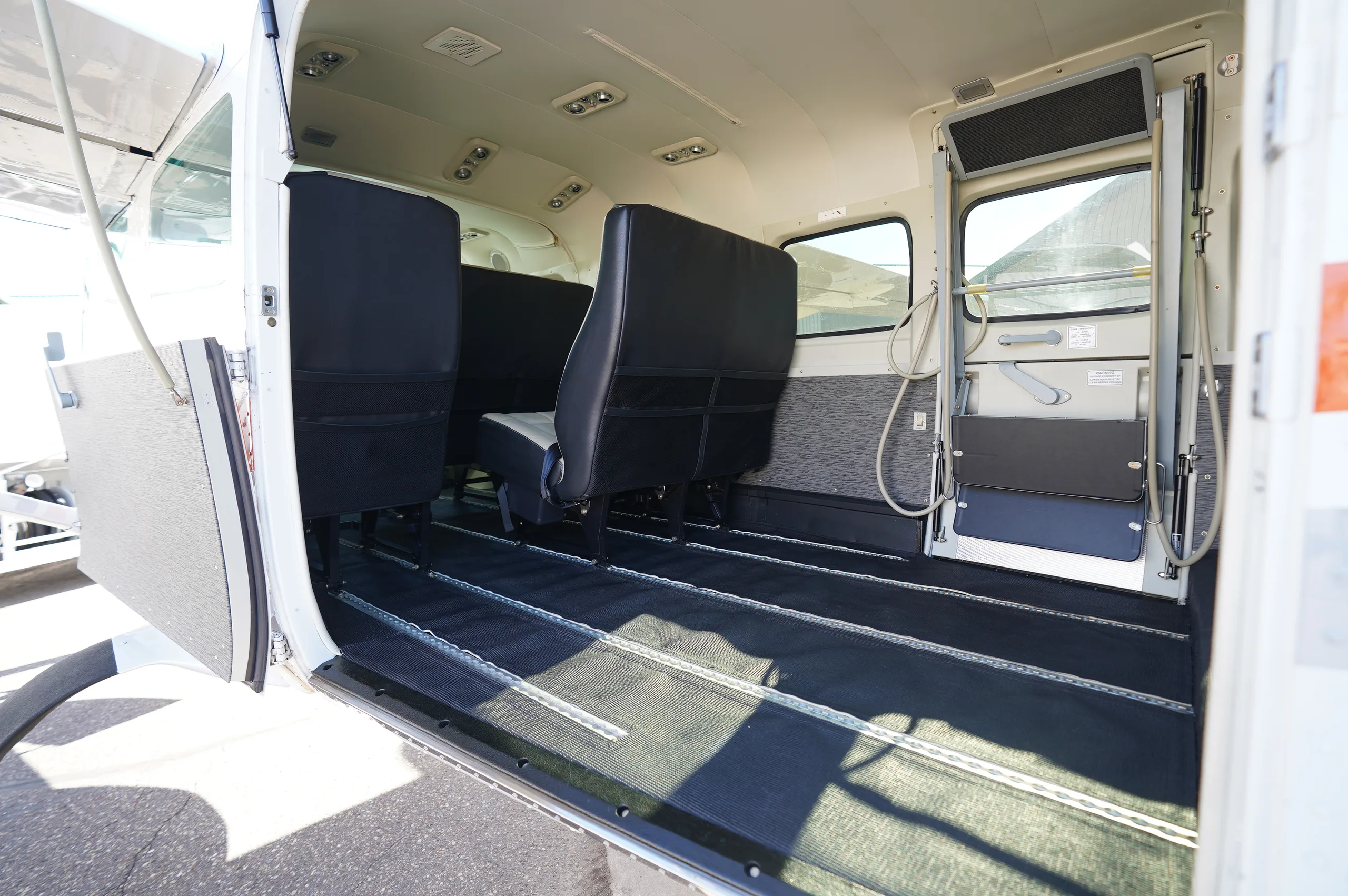 The aircraft's interior cabin with the side door open, showing cargo rails on the floor and some seats removed.