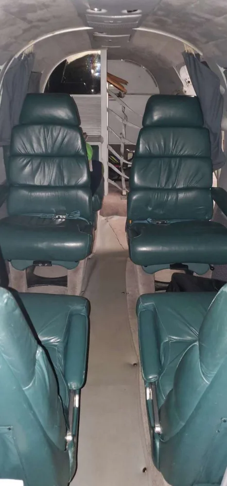 The interior cabin of an aircraft, showing two rows of dark green leather seats facing each other.