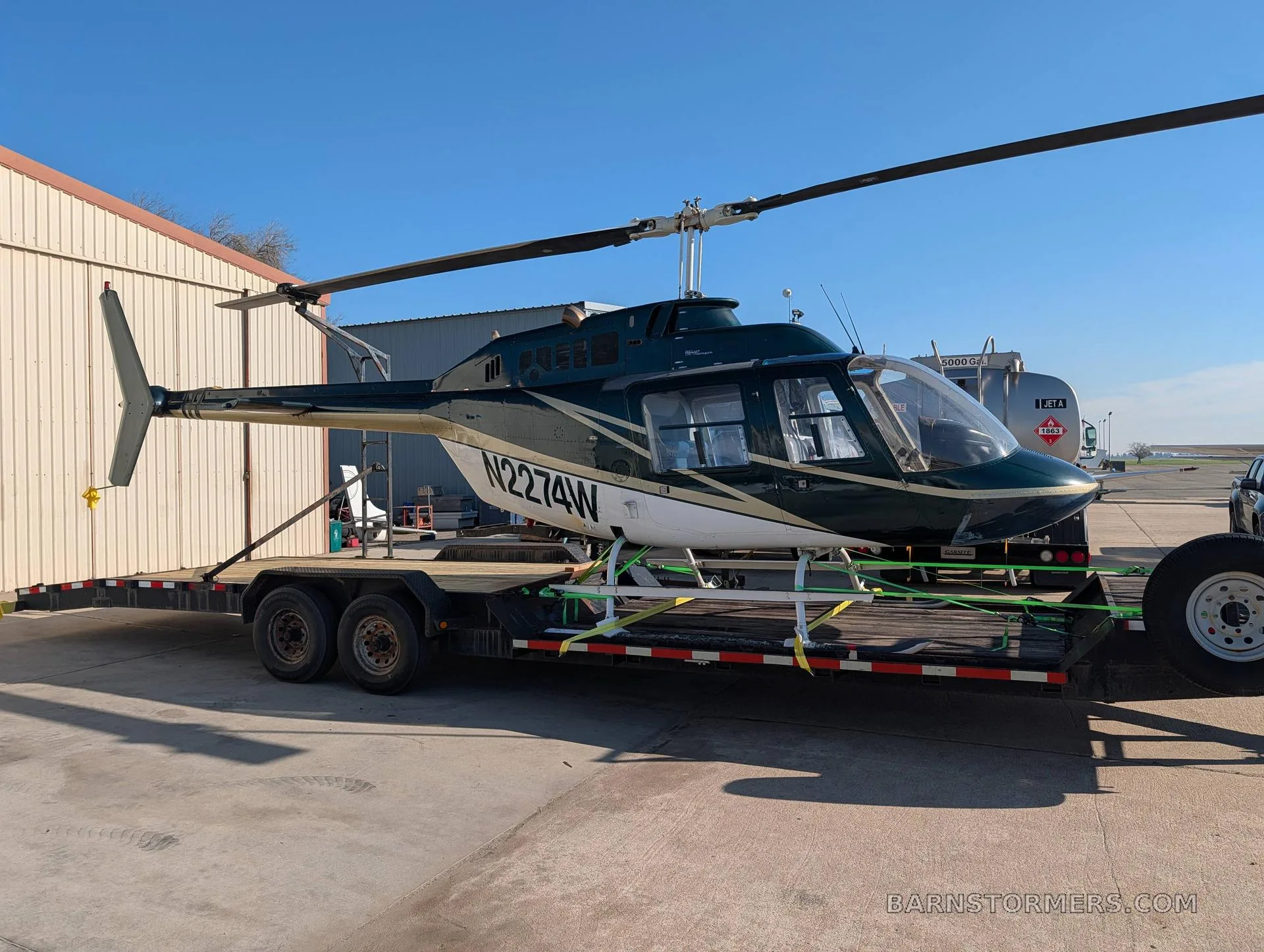 A dark green and white Bell 206 JetRanger helicopter with registration N2274W is secured on a flatbed trailer outdoors.