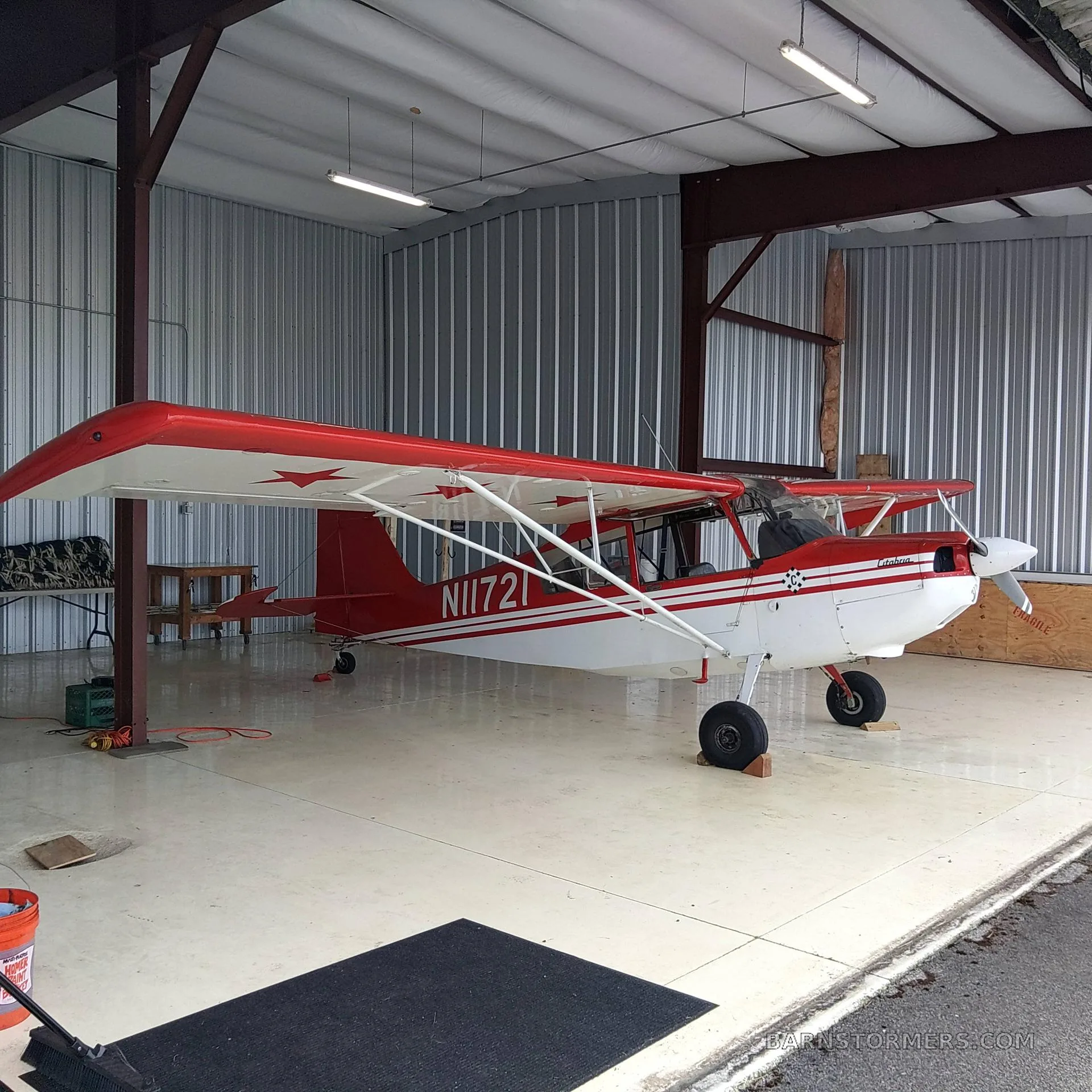 A red and white Citabria N11721 aircraft with stars on the wing, parked inside a metal hangar.