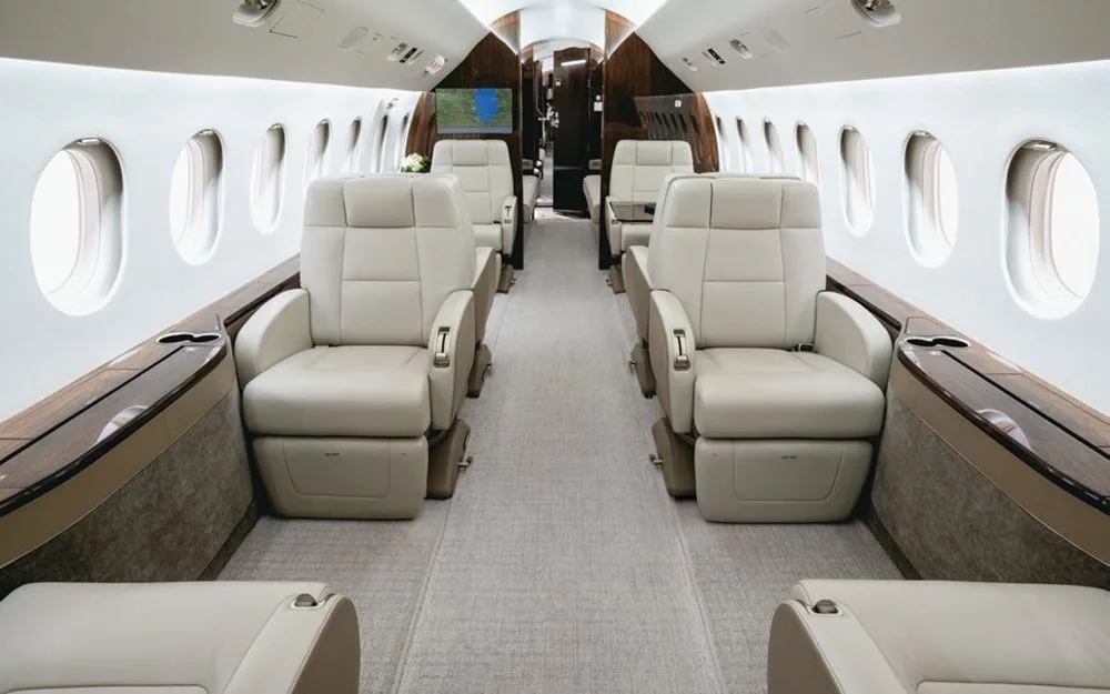 The luxurious cabin interior of a Dassault Falcon 900EX, featuring light-colored leather seats and dark wood accents.