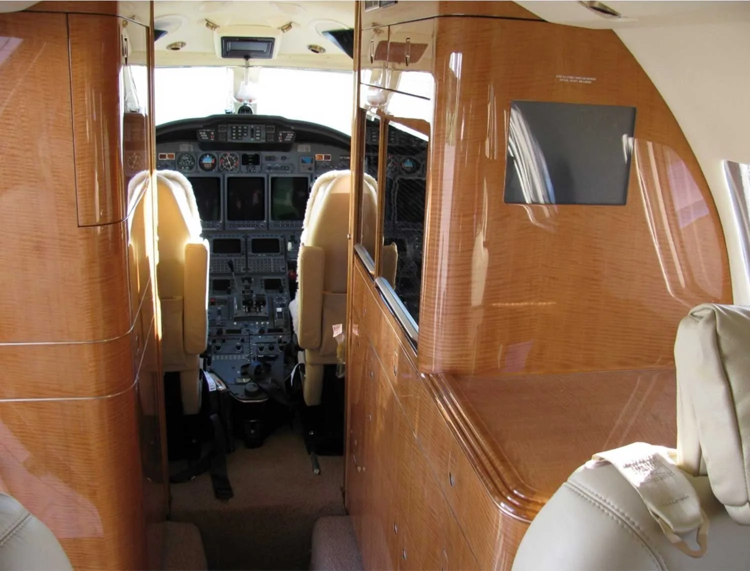View from the aircraft cabin looking forward into the cockpit, showing polished wood paneling and beige seats.
