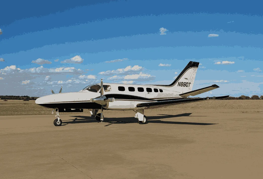 A white twin-engine Cessna 414 Chancellor with black stripes is parked on a tarmac under a blue sky.