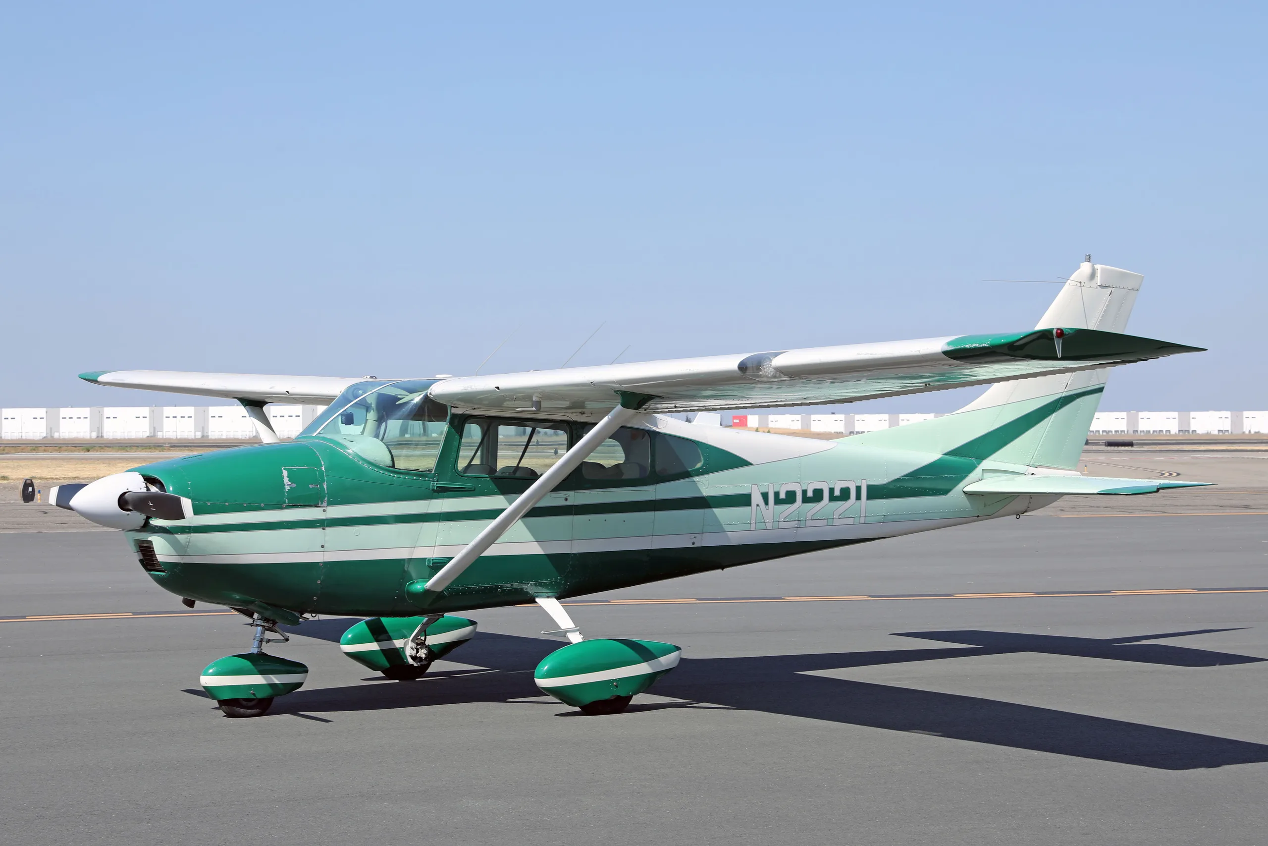 A side view of a green and white Cessna 182 Skylane N2221 on an airfield tarmac.