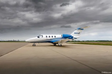 A white business jet with blue and silver stripes is parked on a tarmac under a cloudy sky.
