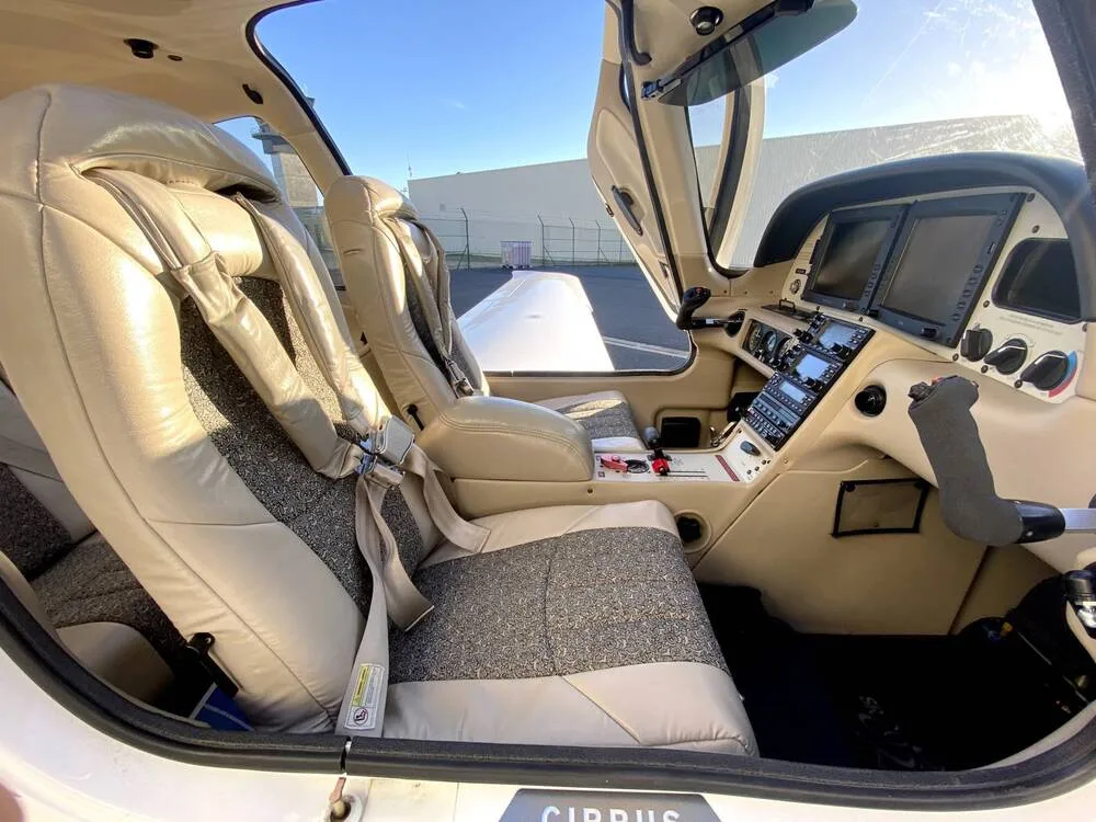 The cockpit and front cabin of a Cirrus SR22, showing beige leather seats with grey fabric inserts and the instrument panel.