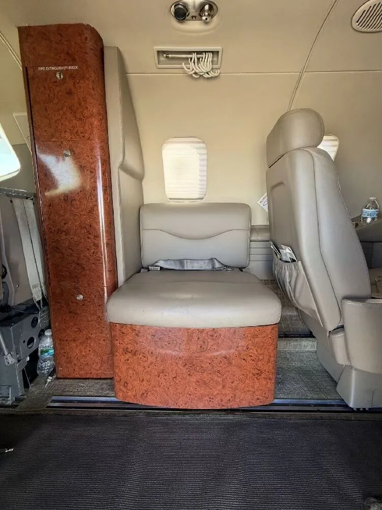 A view inside the aircraft cabin showing a tan leather seat and a wood-grain cabinet.