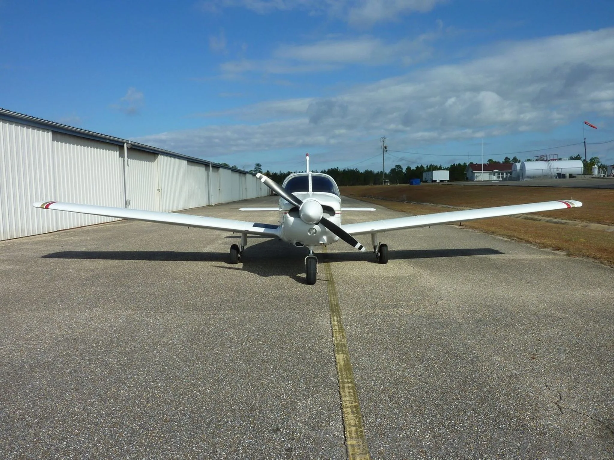 A white Piper Archer II aircraft with red and gold stripes parked on an airfield tarmac under a blue sky.